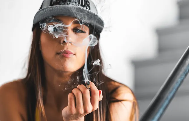 Young woman smoking with a cap, smoke obscuring part of her face